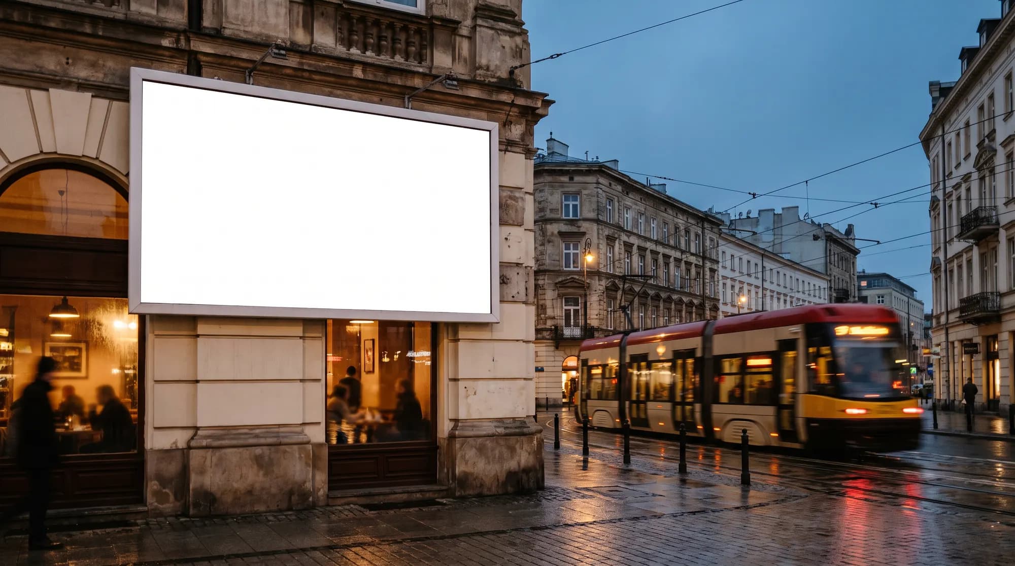 Wieczorna ulica w Warszawie z pustym białym billboardem na kamienicy, przejeżdżającym tramwajem i oświetlonymi oknami kawiarni